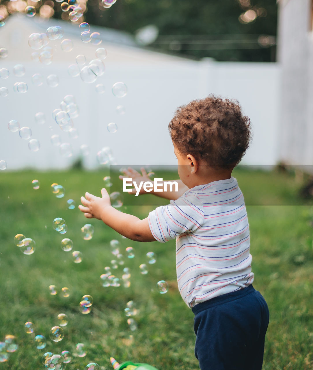 Diverse mixed race toddler boy outdoors on a nice summer day having fun playing with bubbles