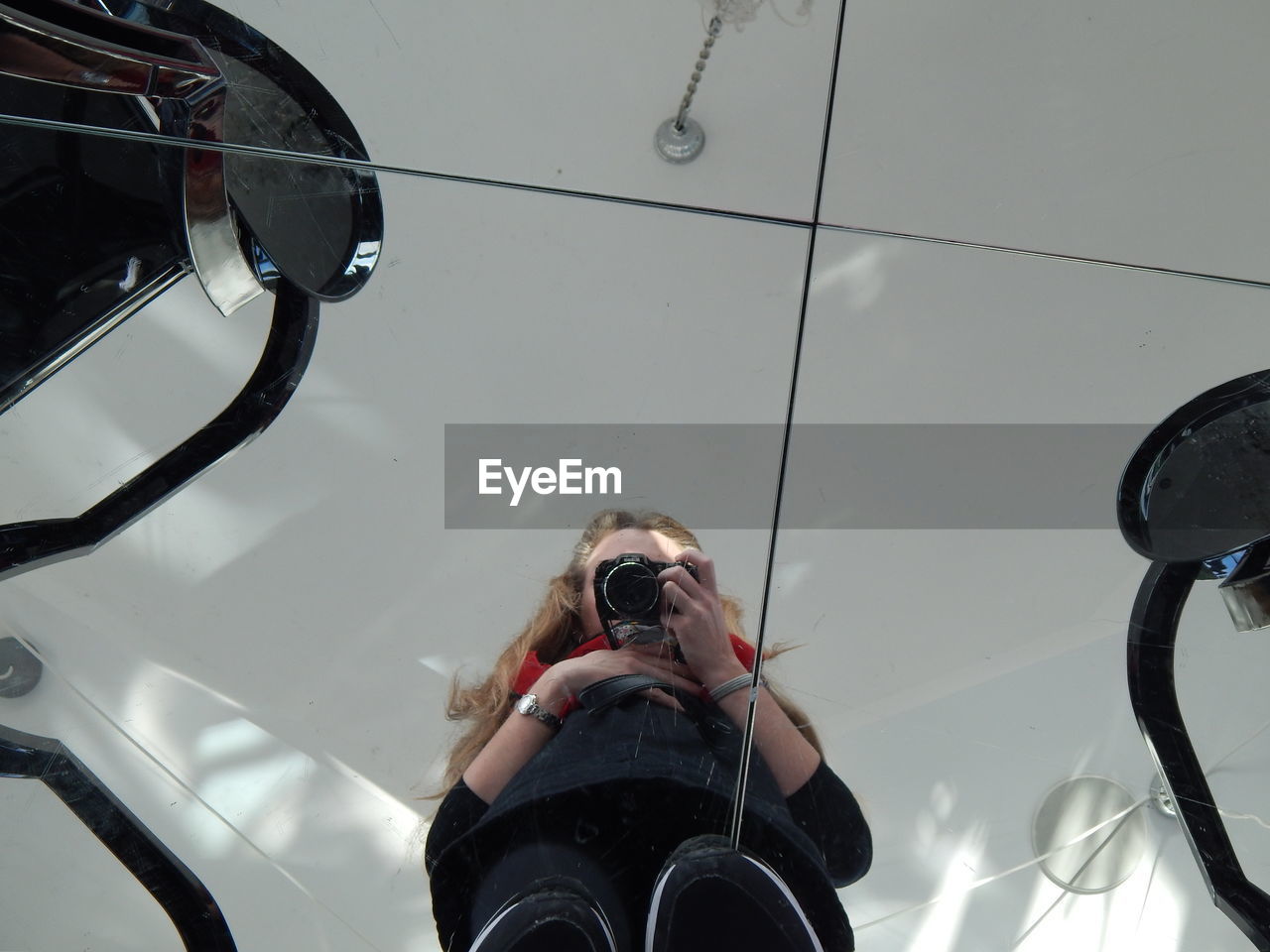 High angle view of young woman photographing with camera reflecting on tiled floor