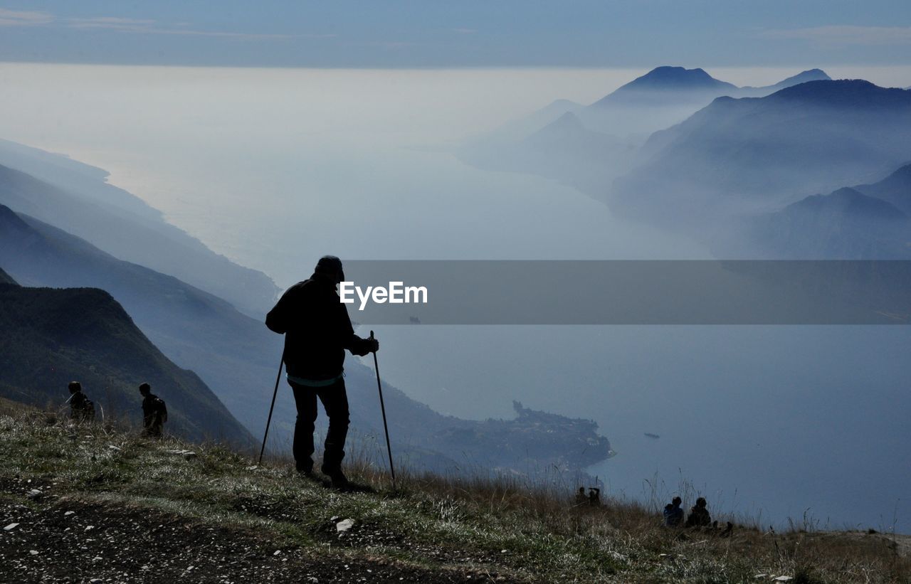 REAR VIEW OF MEN STANDING ON MOUNTAINS AGAINST SKY