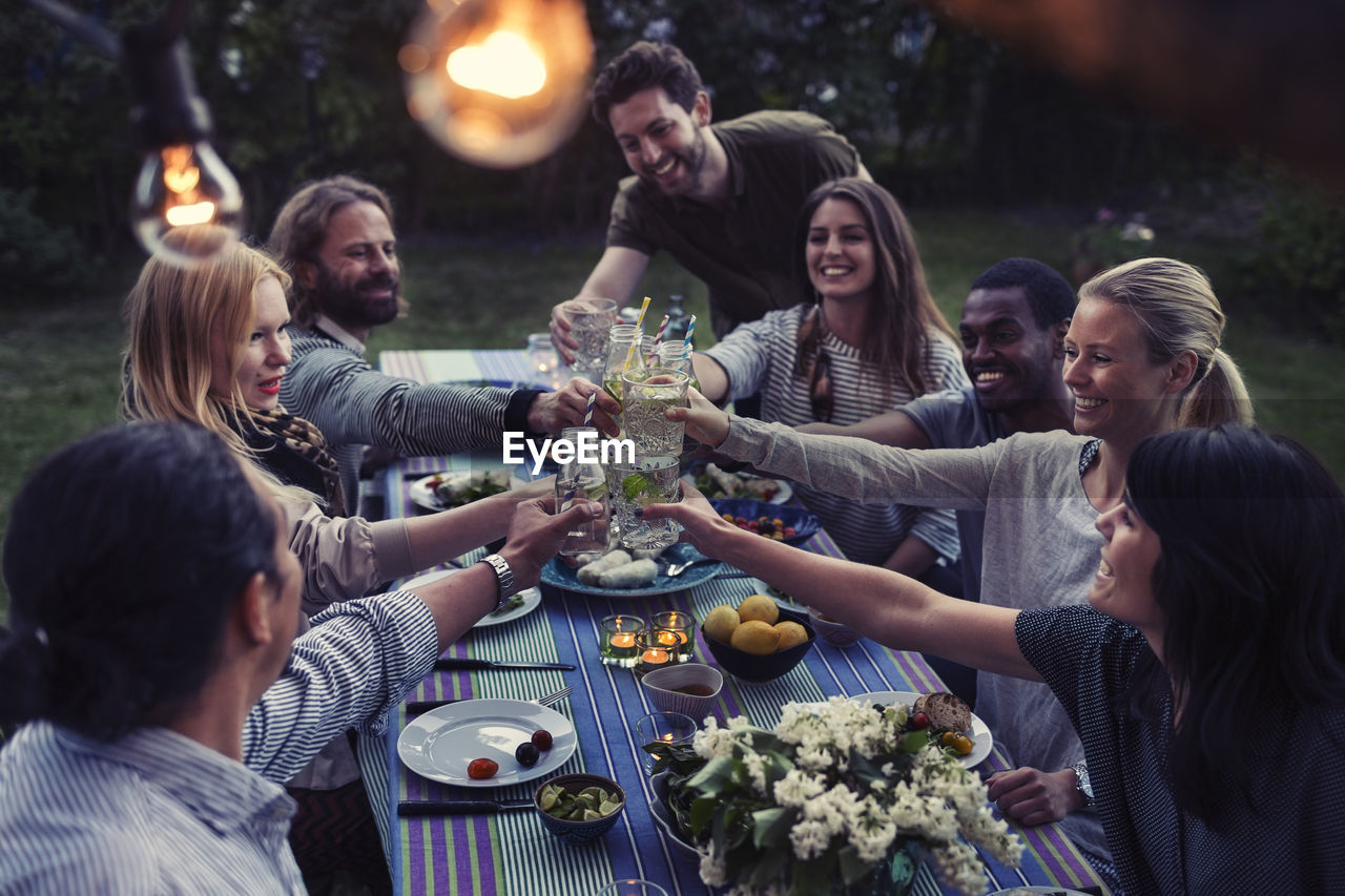 Happy multi-ethnic friends toasting drinks at dinner table in yard