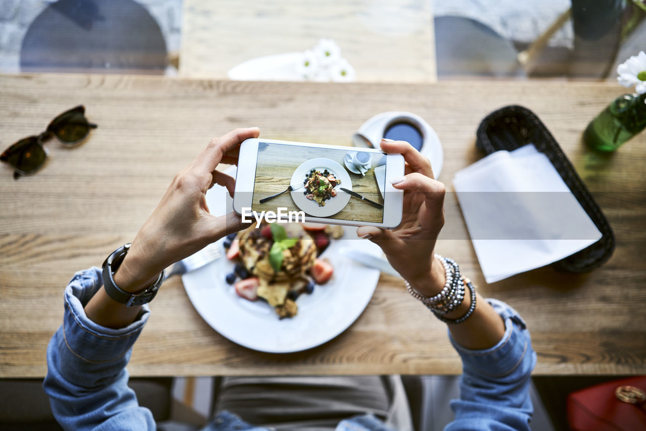 Overhead view of woman taking smartphone picture of pancakes in cafe