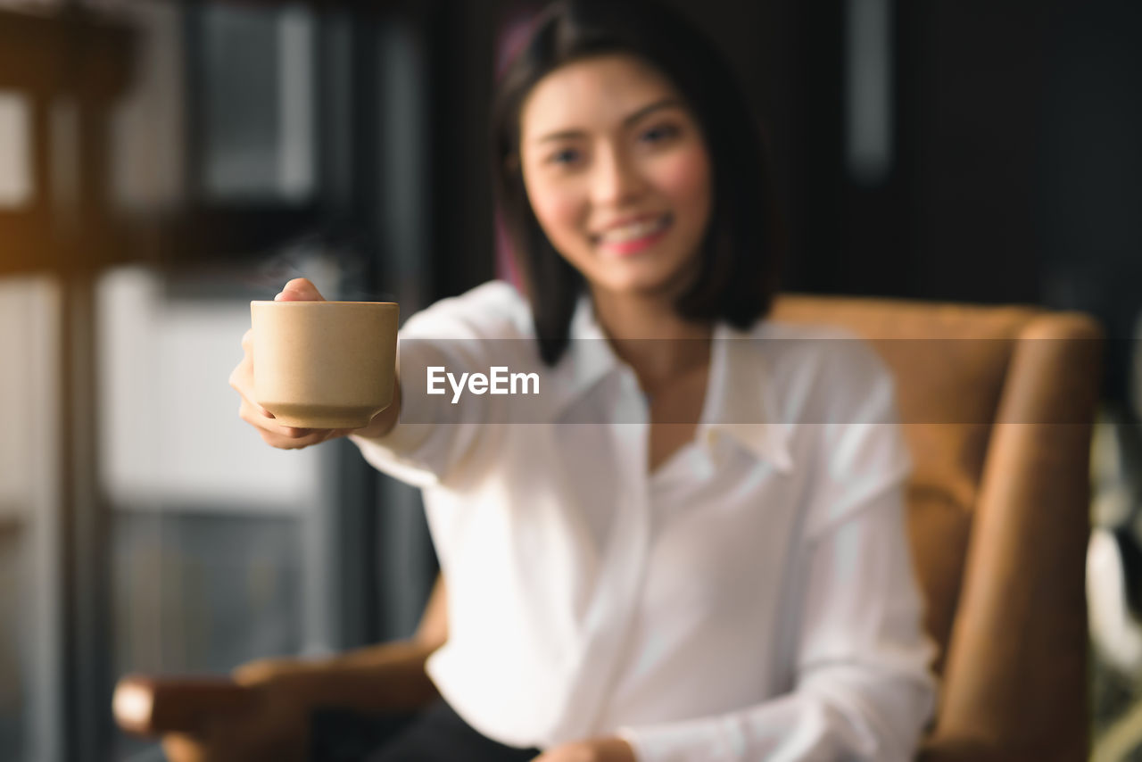 An asian woman holds a cup of coffee and gives it to invite to drink together.