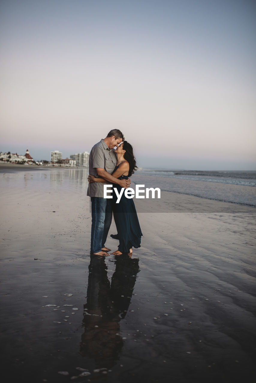 Barefoot loving mid-40's couple on beach embracing face to face negative space