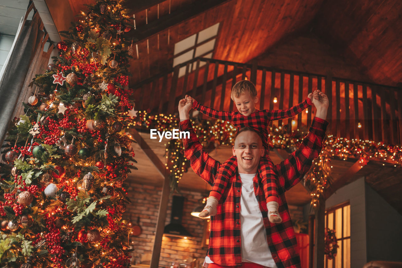 Candid authentic happy dad and son in red plaid pajamas fooling around at wood lodge xmas decorated