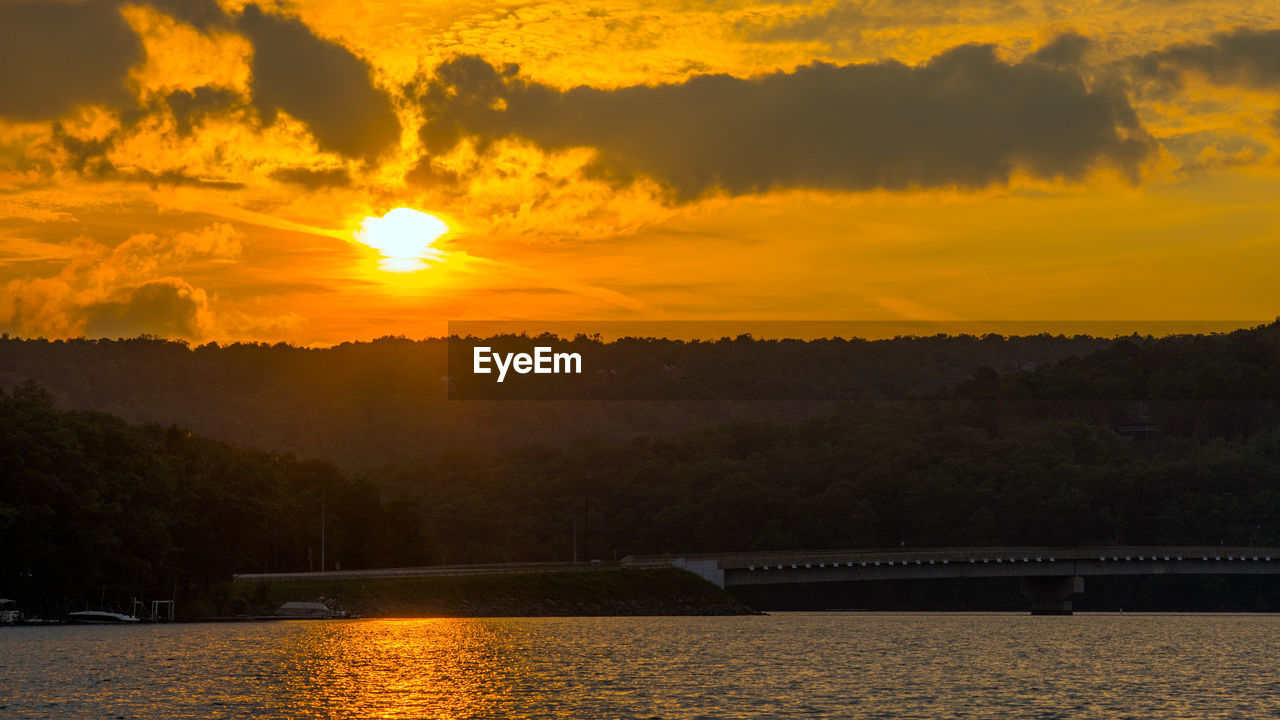 SCENIC VIEW OF RIVER BY SILHOUETTE TREES AGAINST ORANGE SKY