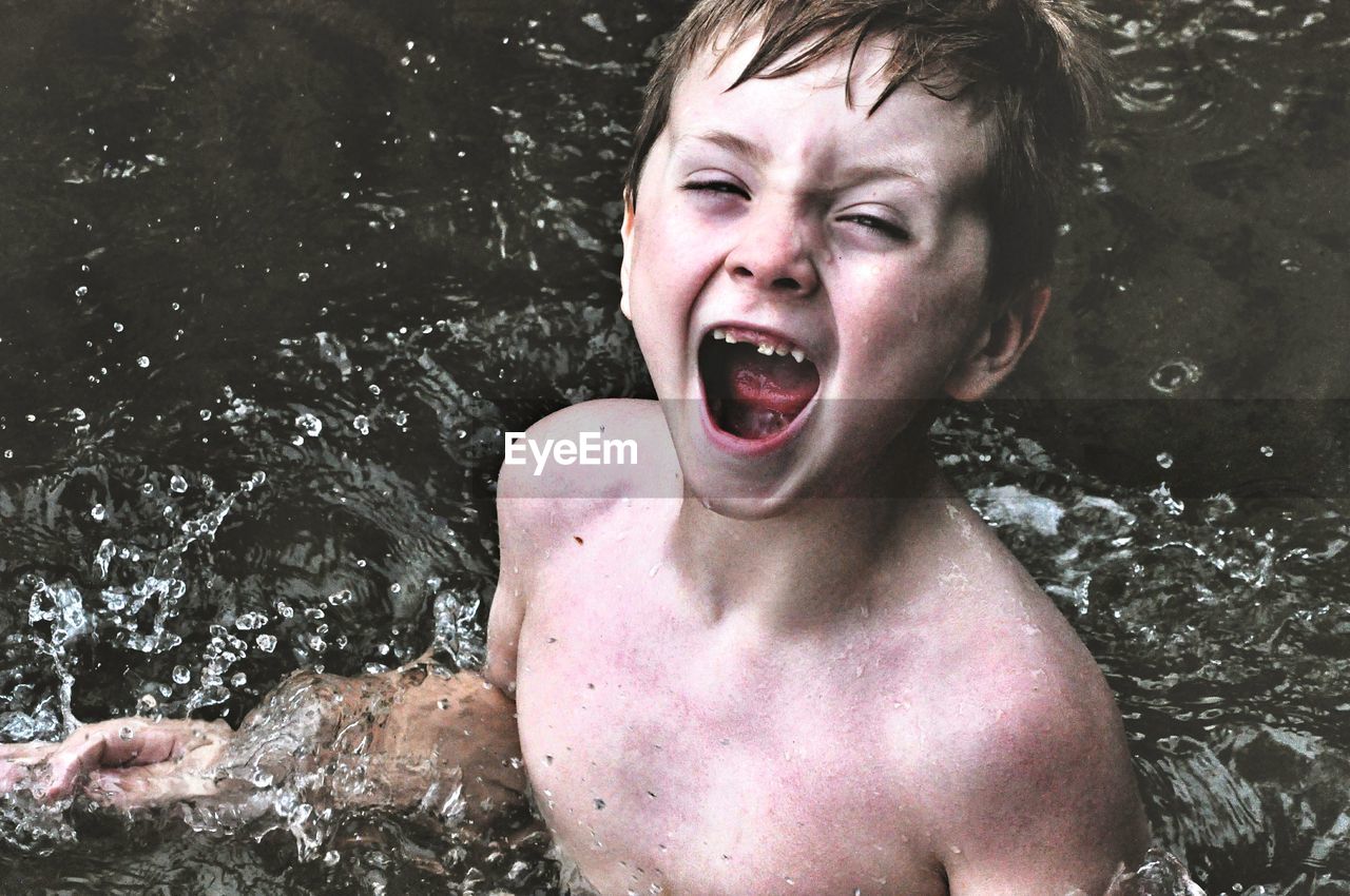 Portrait of shirtless boy shouting while swimming in river