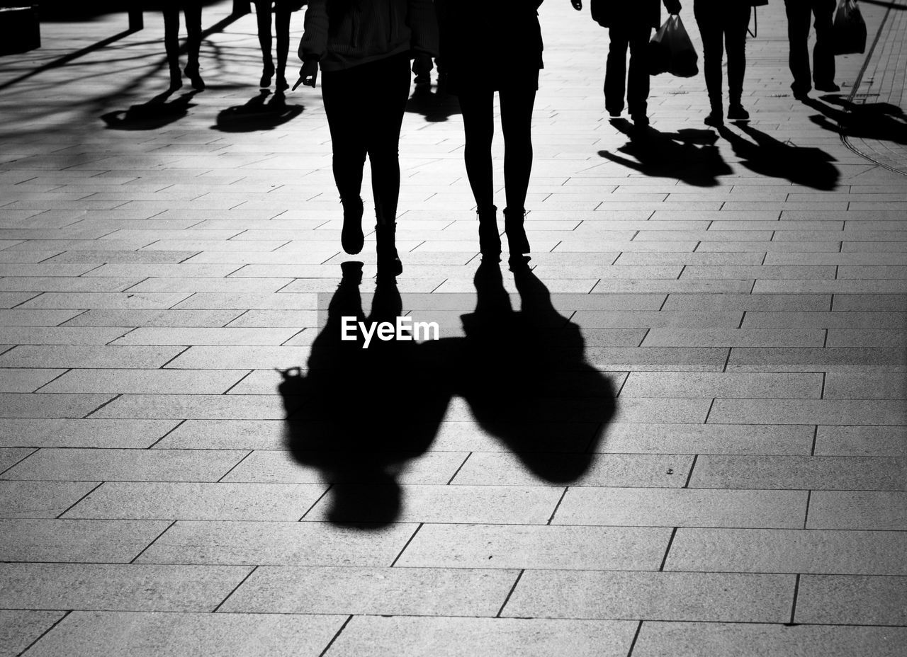 Low section of silhouette people walking on street during sunny day