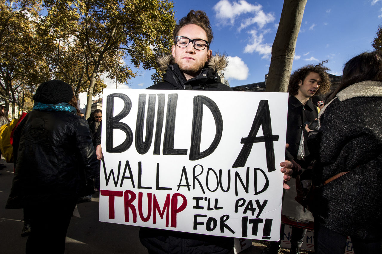 PEOPLE STANDING BY SIGN AGAINST TREE