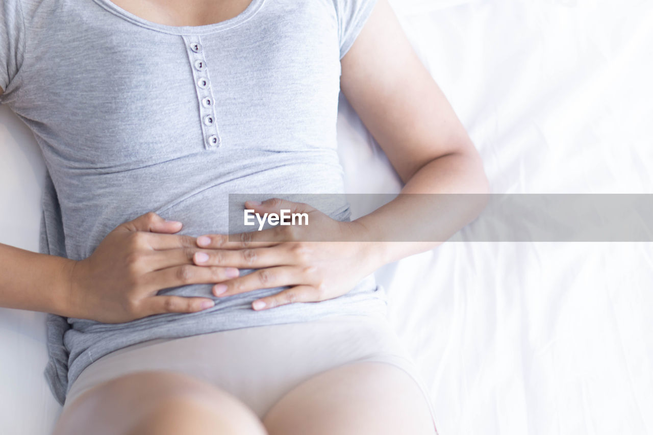 Midsection of woman holding stomach resting on bed