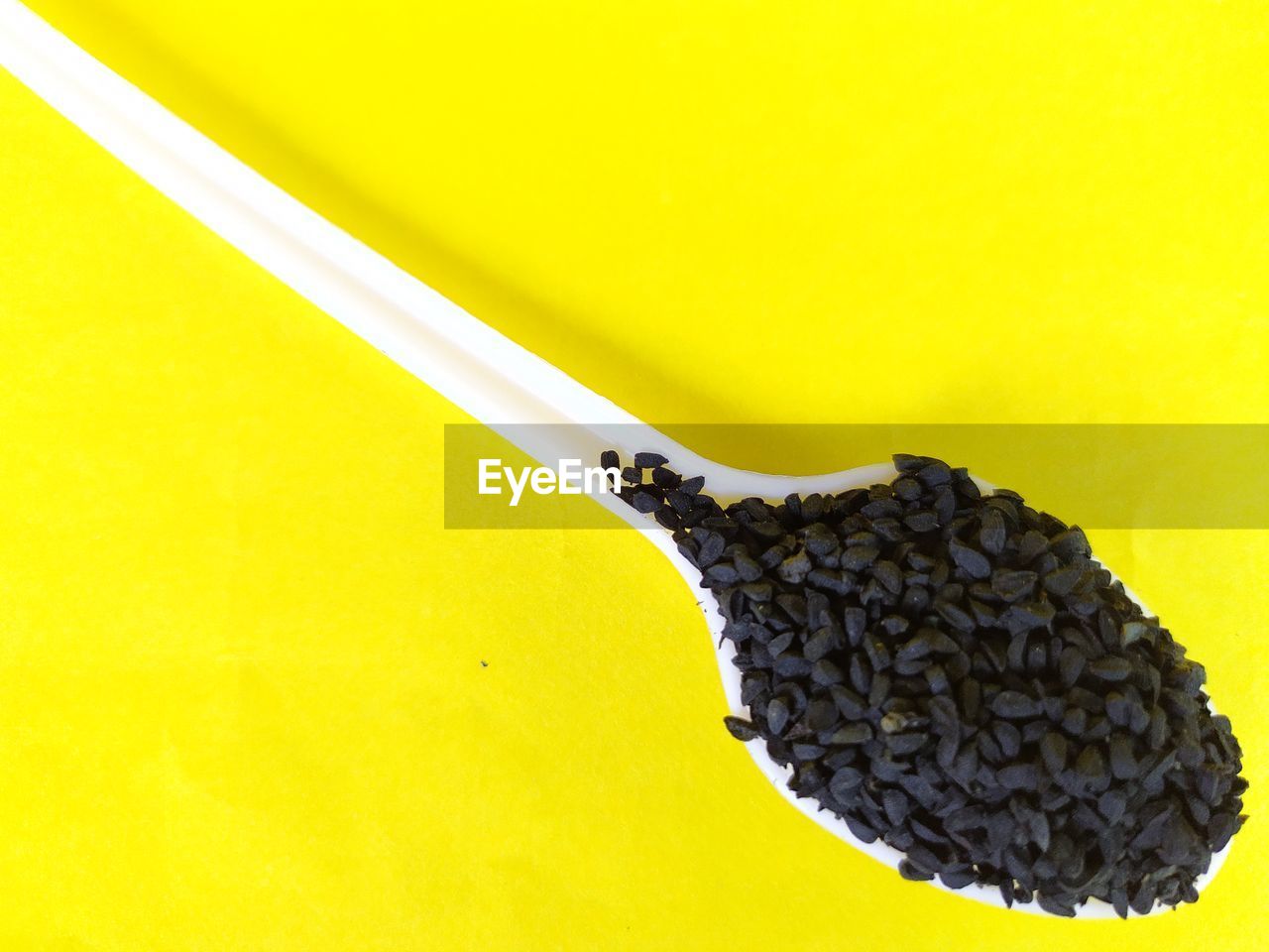 Black cumin seeds on spoon, yellow background.