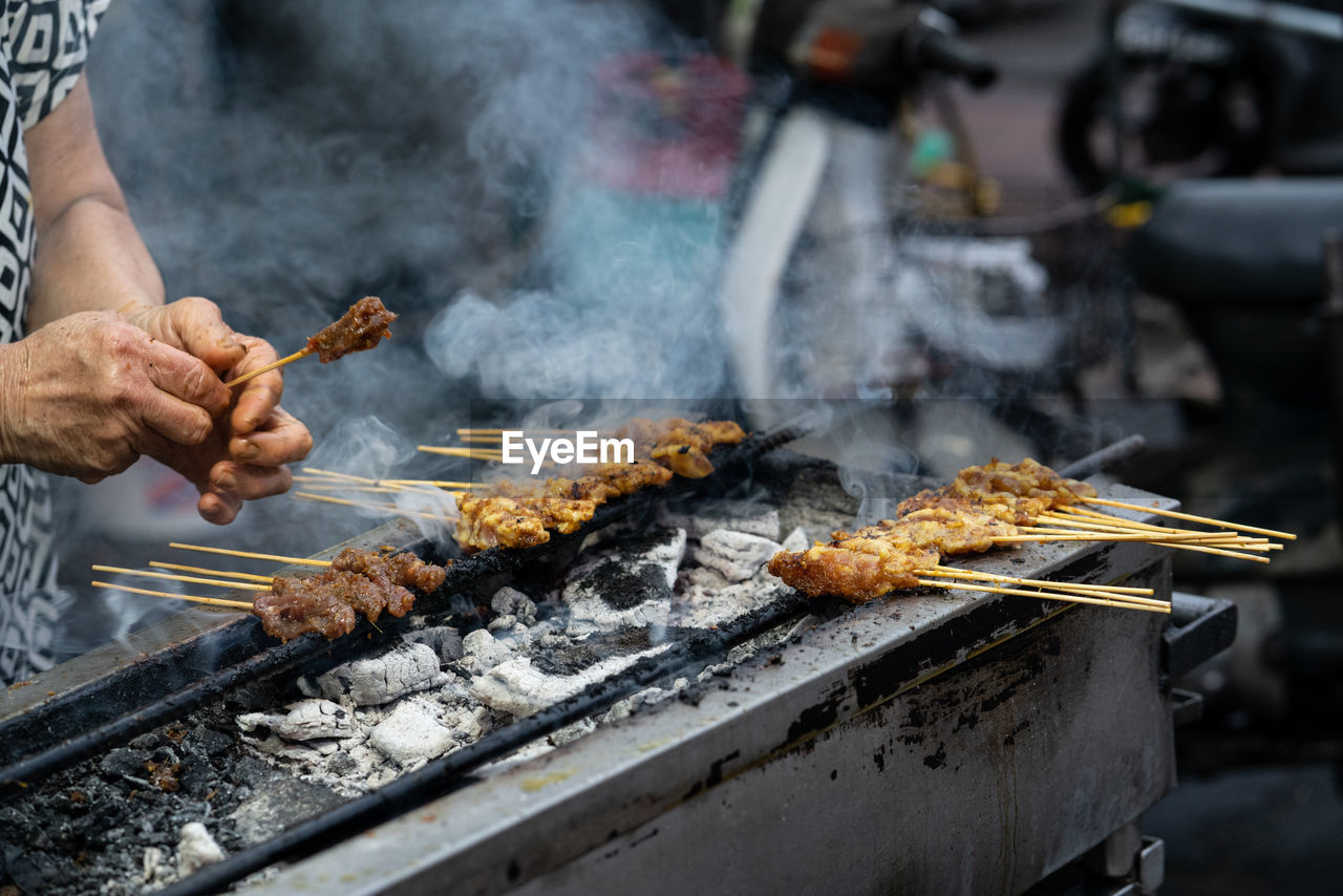 MAN PREPARING FOOD ON BARBECUE GRILL AT MARKET