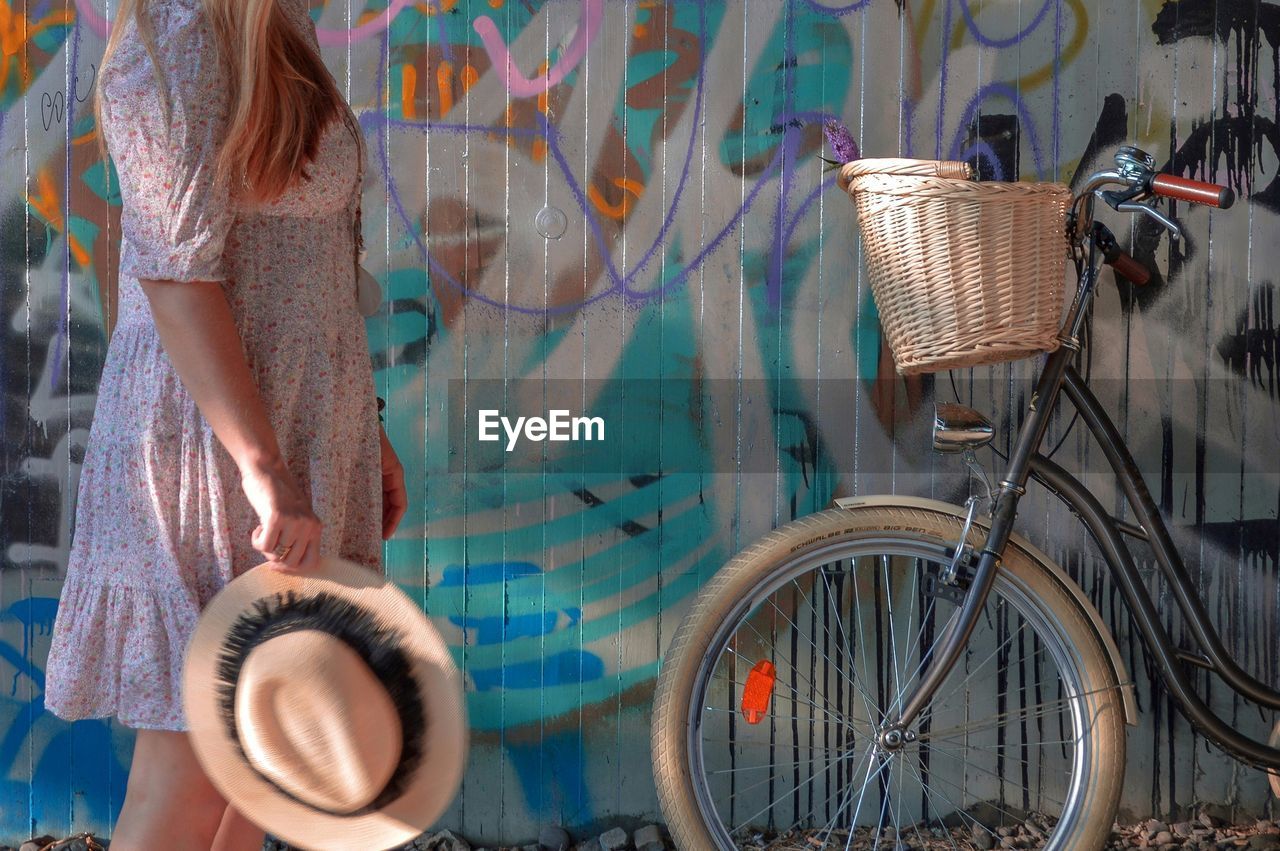 Midsection of woman holding hat while standing by bicycle