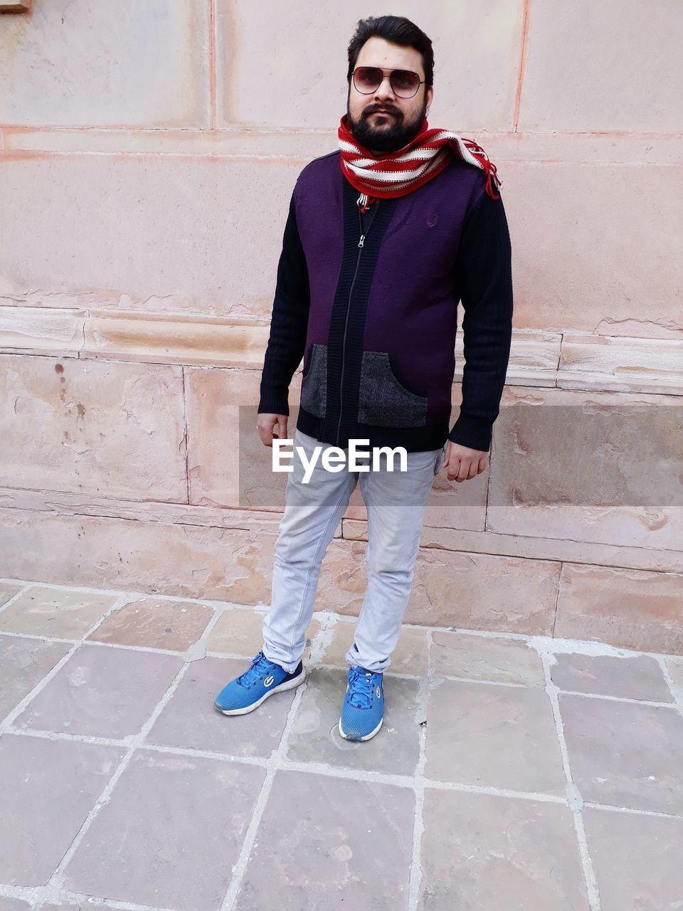 PORTRAIT OF YOUNG MAN STANDING ON FOOTPATH AGAINST WALL