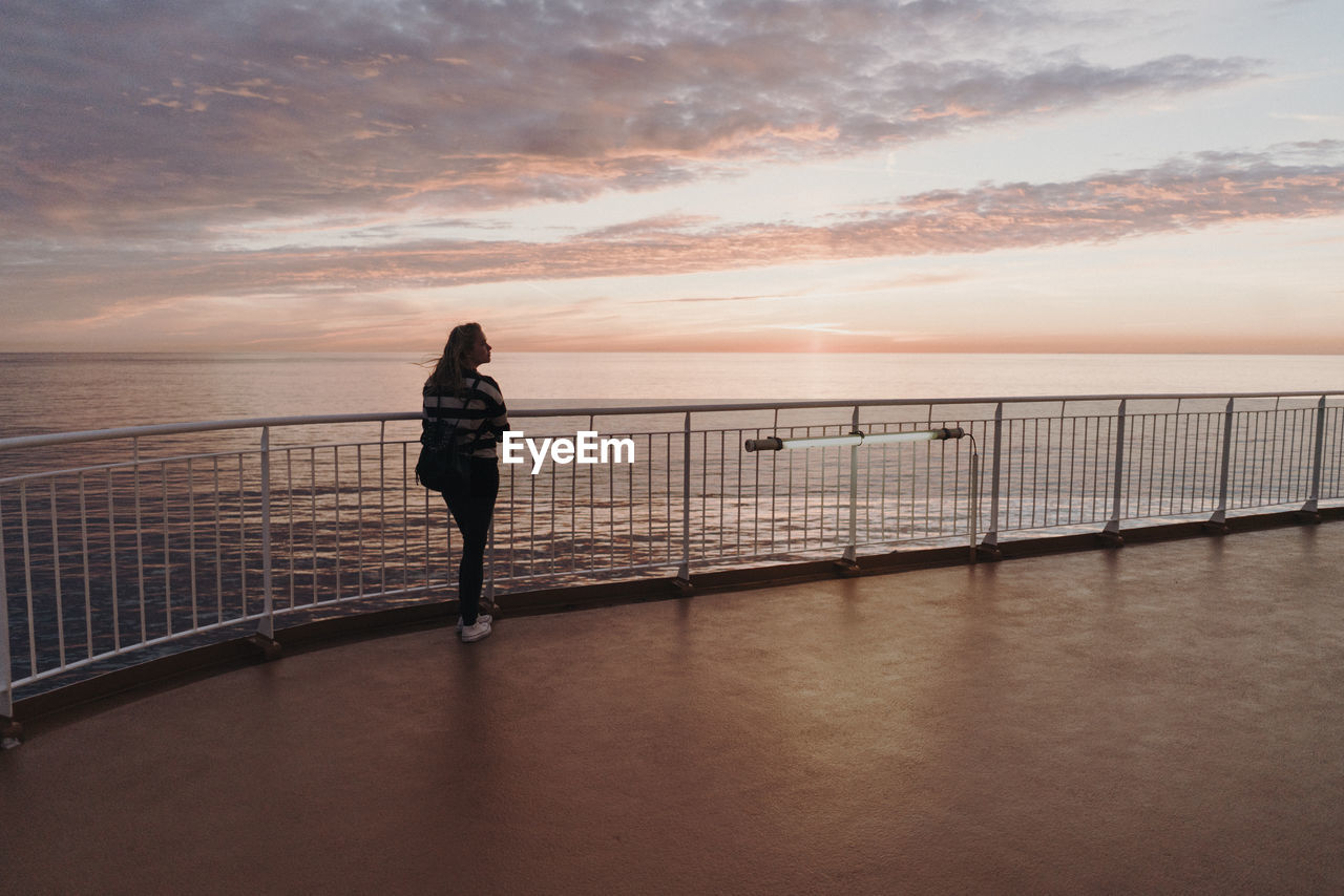 REAR VIEW OF WOMAN STANDING BY RAILING AGAINST SEA