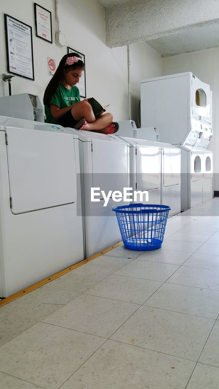 Girl reading book while sitting on washing machine