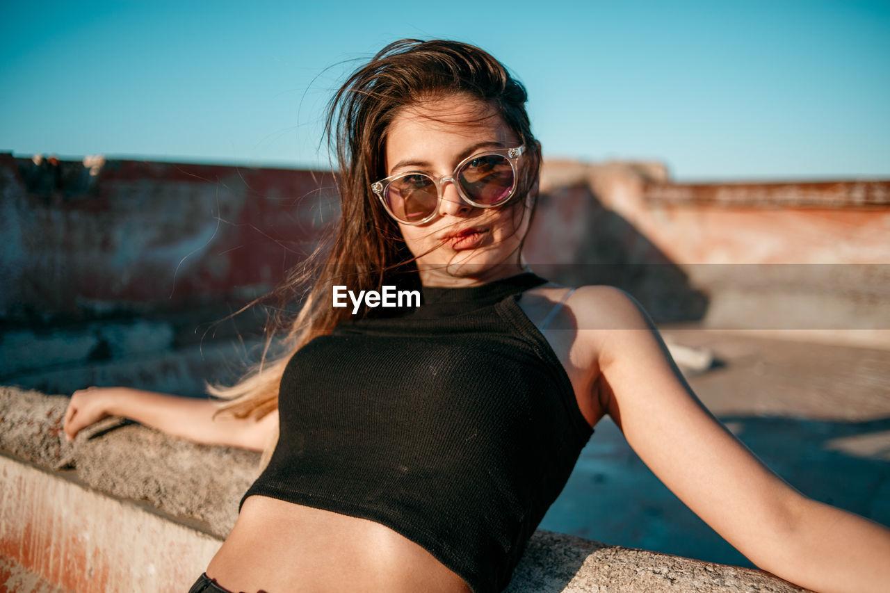 PORTRAIT OF YOUNG WOMAN WEARING SUNGLASSES OUTDOORS