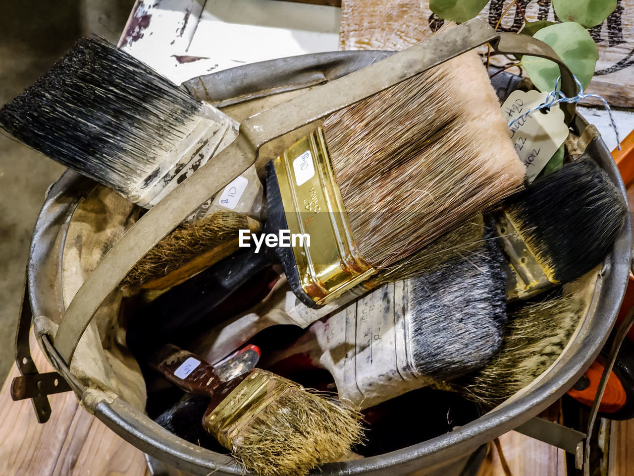 HIGH ANGLE VIEW OF PAINTBRUSHES IN CONTAINER ON WOODEN FLOOR