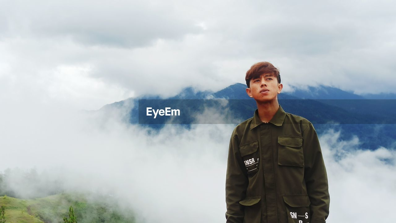 Portrait of young man standing on mountain against sky