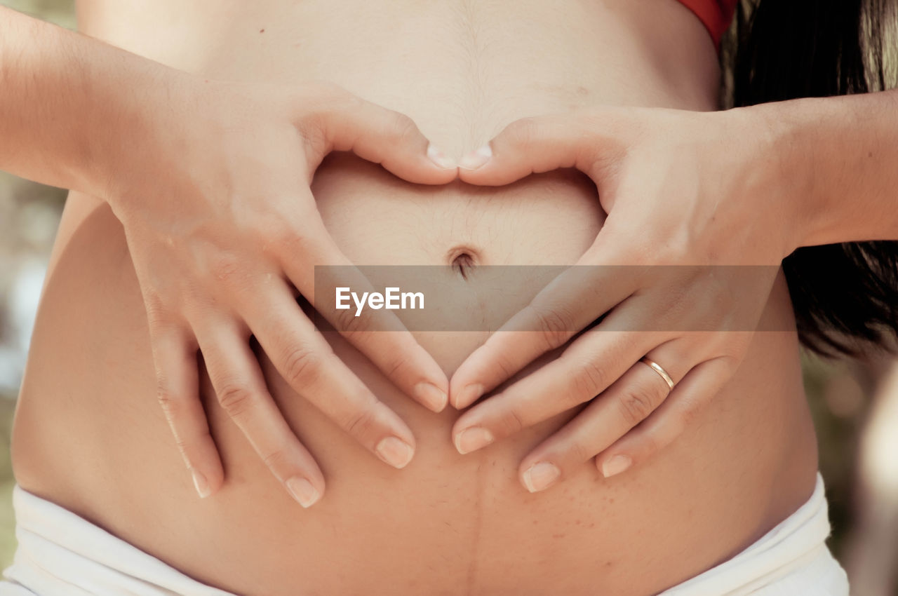 Midsection of woman holding heart shape with hands