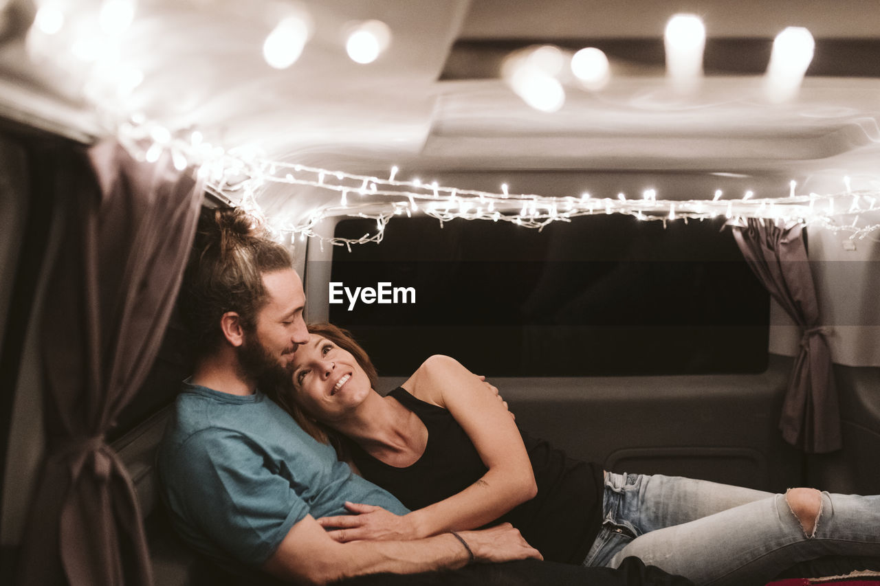 Smiling woman lying with boyfriend in illuminated van at night