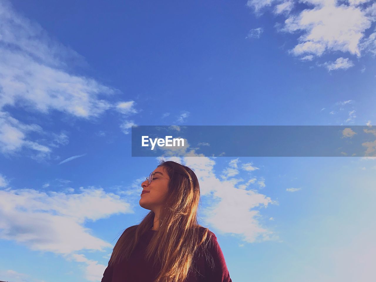 Low angle view of young woman against blue sky