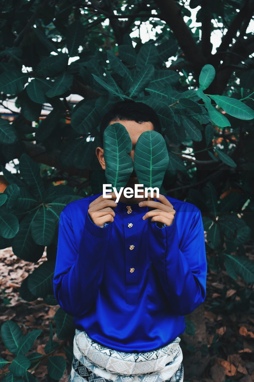 Man covering face with leaves while standing against plants