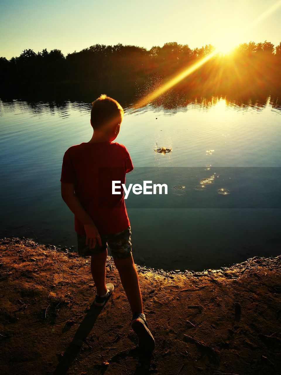 Boy walking against lake during sunset