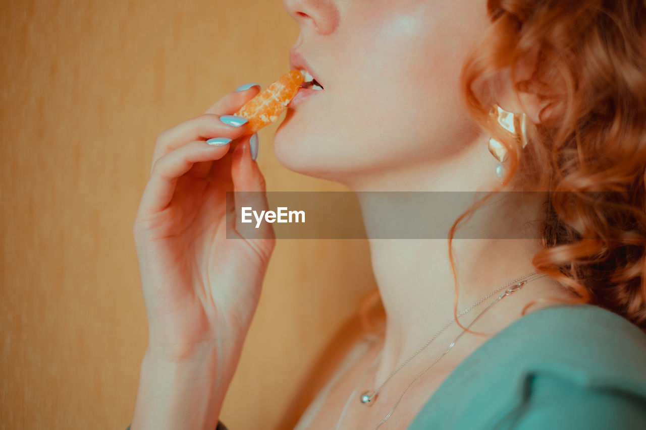 Midsection of young woman eating orange against wall at home