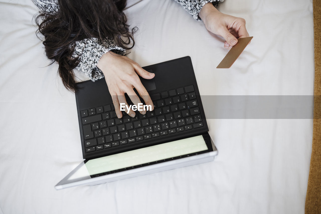 Woman with credit card doing online shopping through laptop on bed