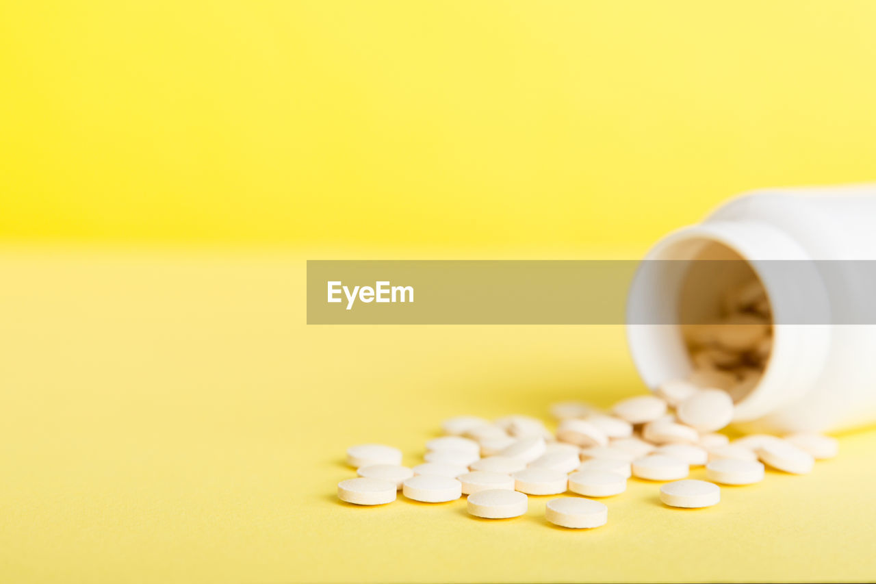 close-up of pills spilling from bottle against yellow background