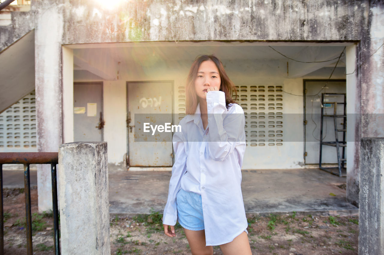 Portrait of young woman standing against building