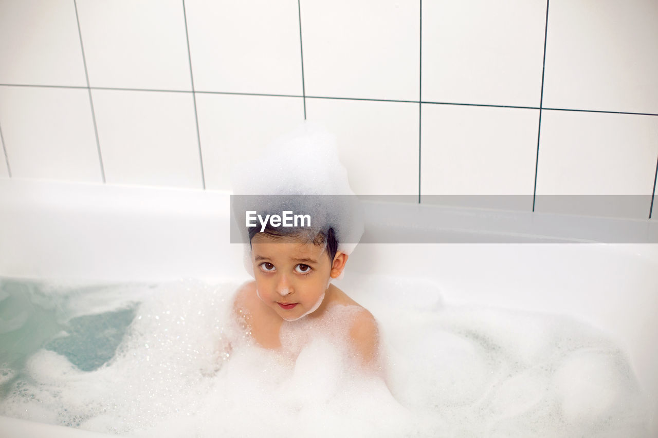 Boy with big eyes a caucasian child bathes in a white bath with foam