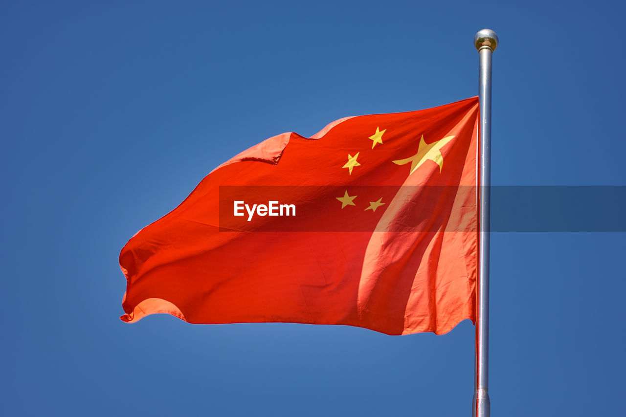 Low angle view of red flag against blue sky