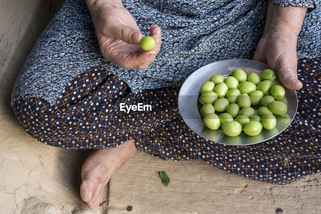 Woman's hand holding a steel plate of green plums