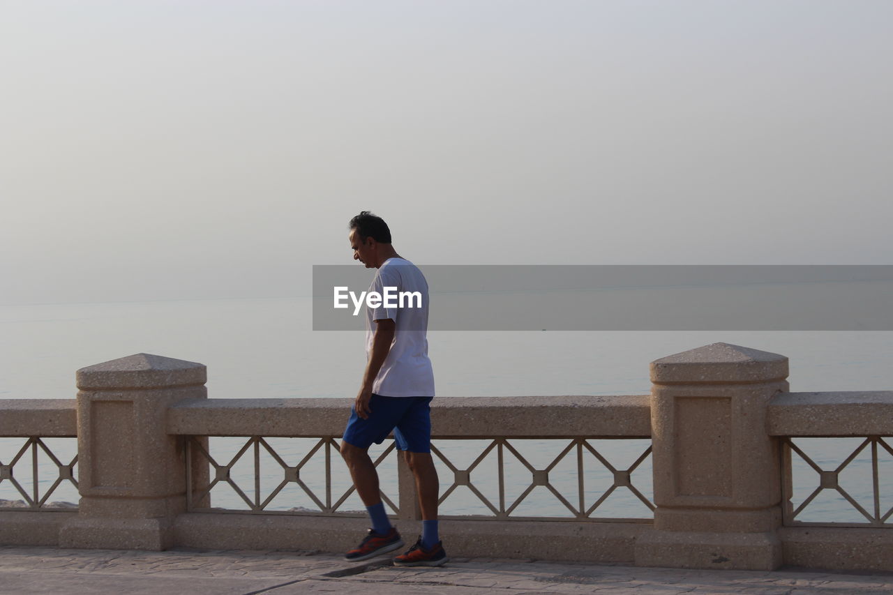 Side view of man walking on promenade against clear sky during sunset