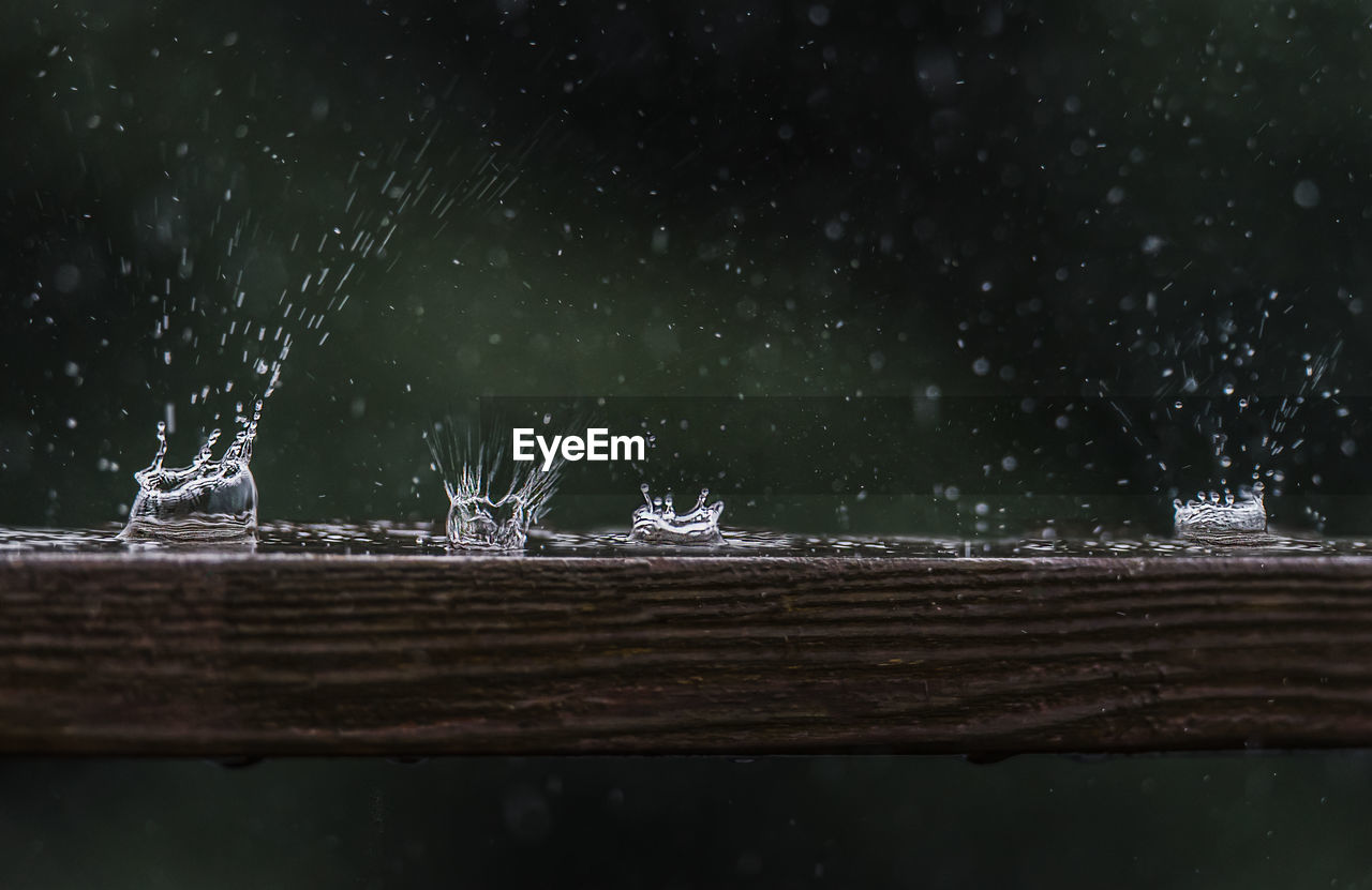 Close up of raindrops hitting a wooden railing with a splash.
