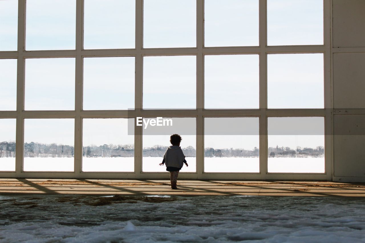 Rear view of child standing on footpath against sky during winter