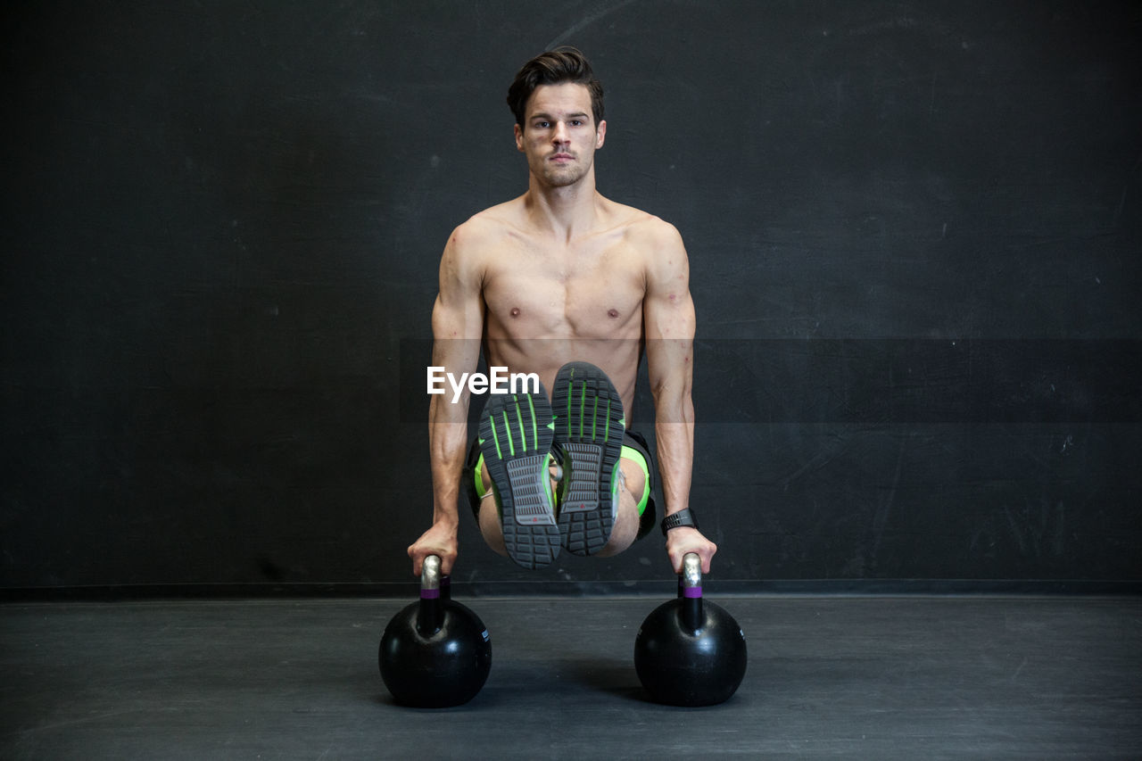 Portrait of shirtless man exercising with kettlebells in gym