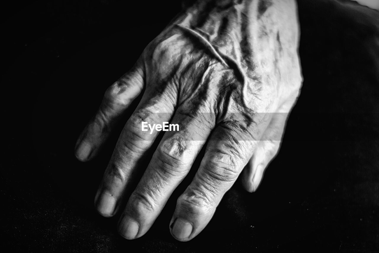 Cropped image of wrinkled hand against black background