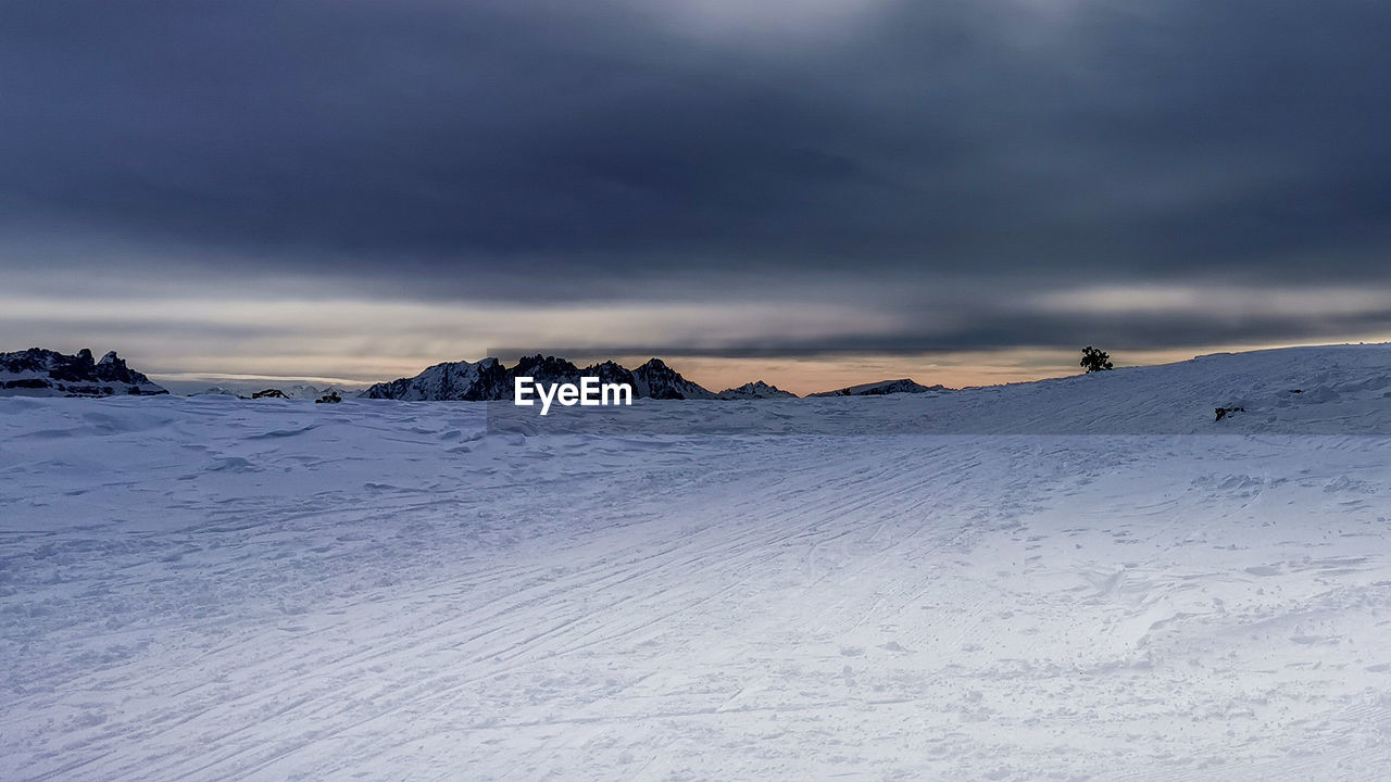 Snow covered landscape against the dolomites and bad weather sky with some pale light