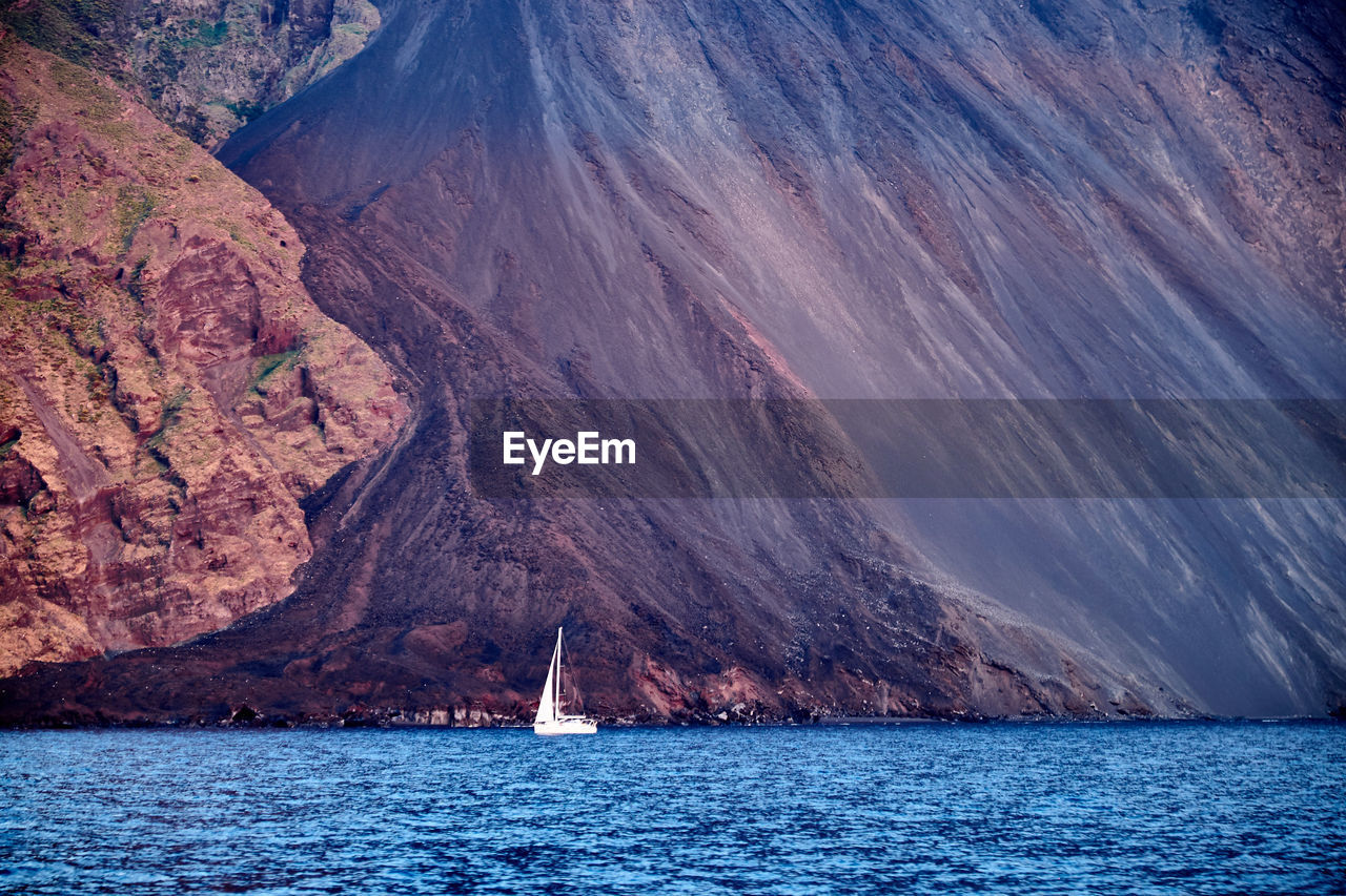 Distant view of sailboat on sea against mountain