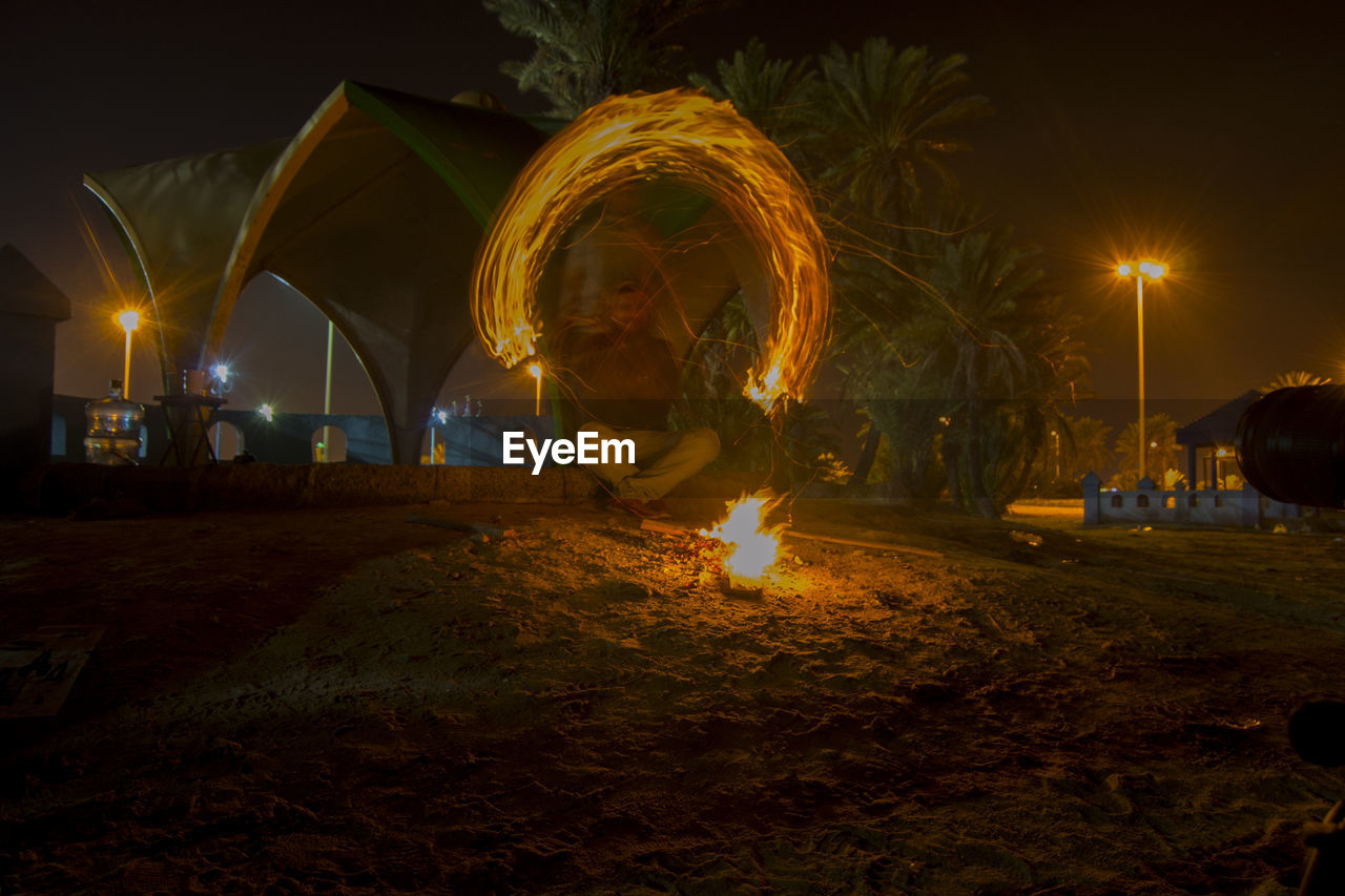 Man sitting at campfire with light painting during night