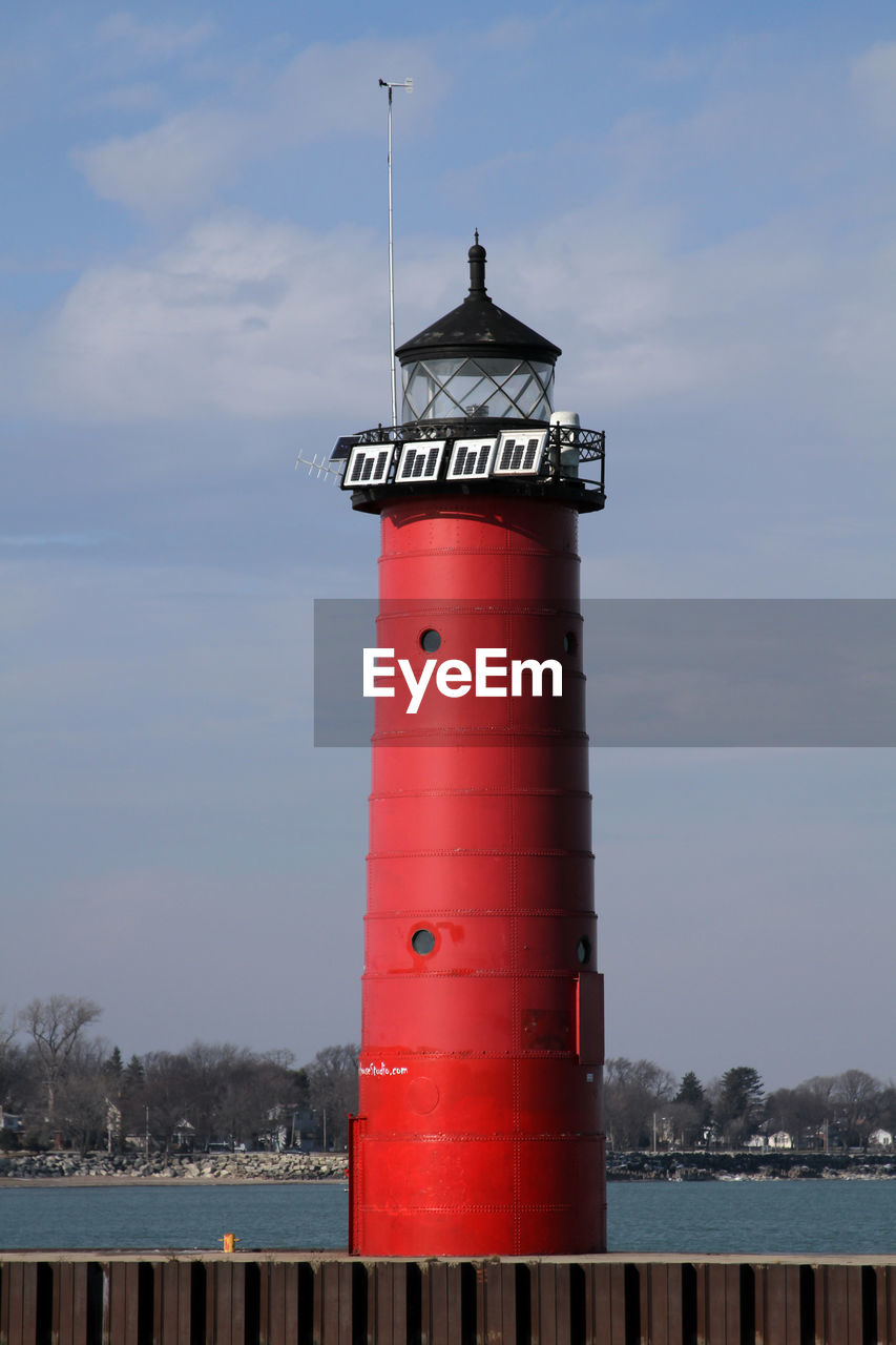 Lighthouse by building against sky