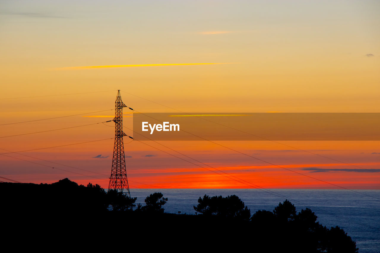 Silhouette electricity pylon by tree against romantic sky at sunset