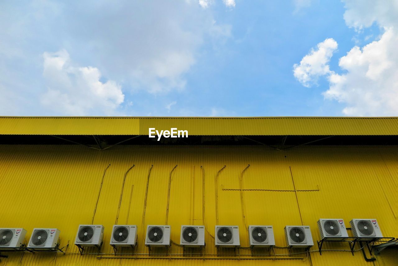 Low angle view of air conditioners on yellow building against sky