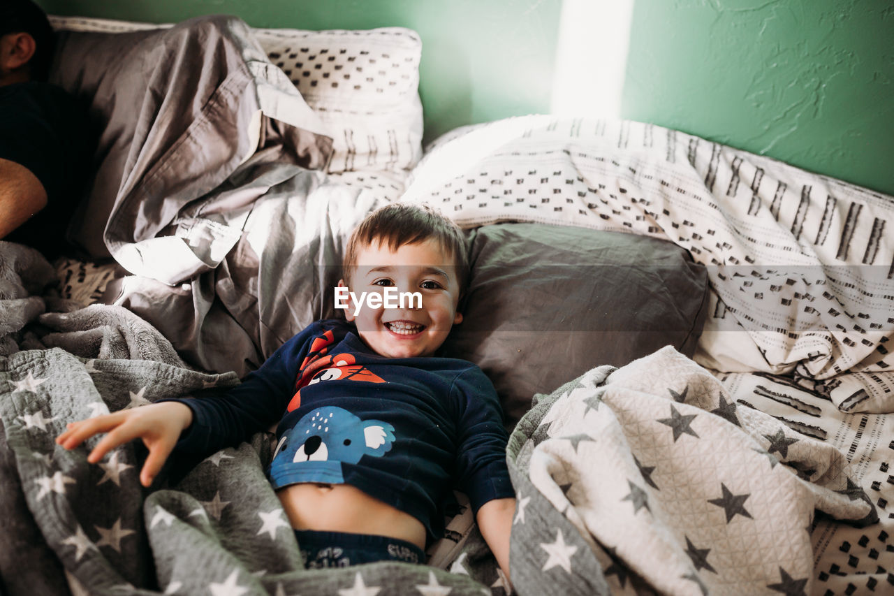 Young boy wearing pjs in bed smiling and looking at camera