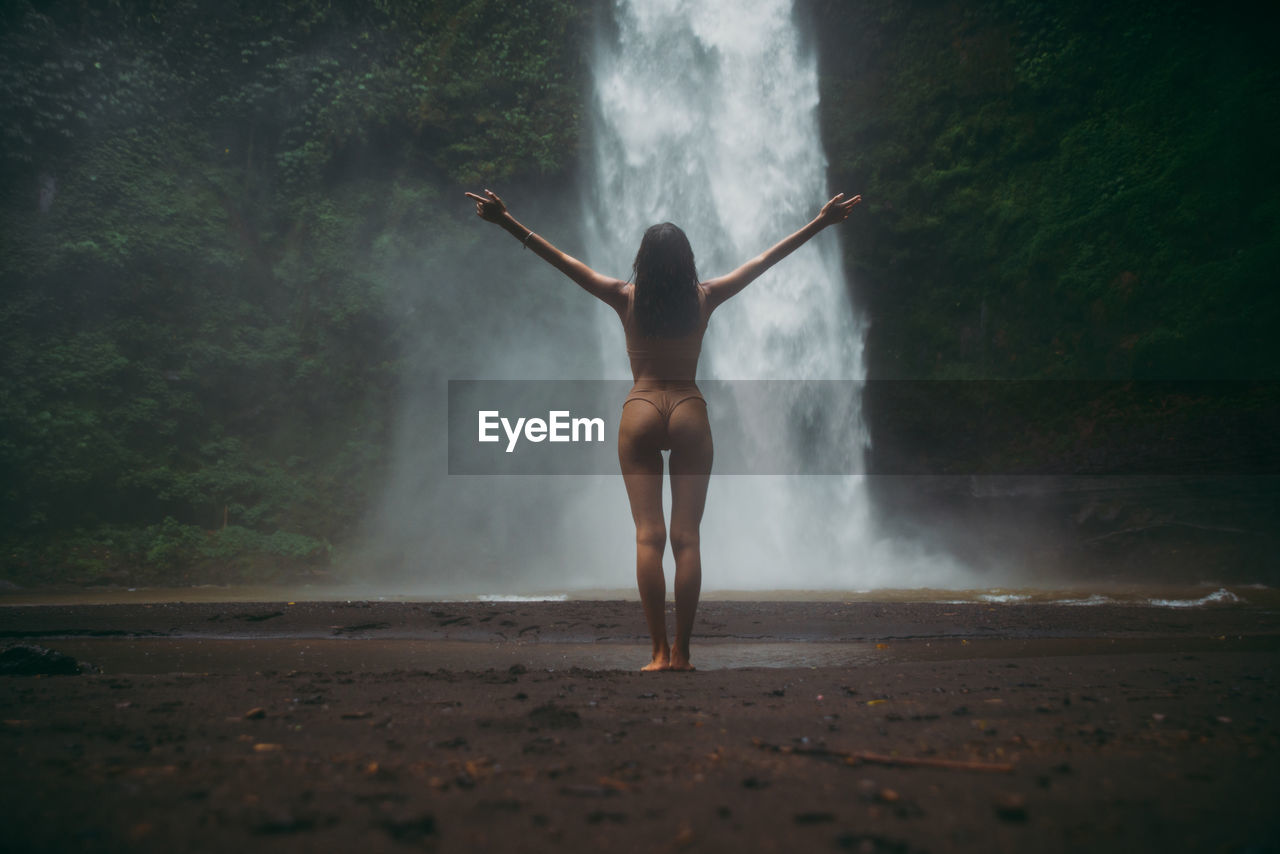 Young woman standing against waterfall