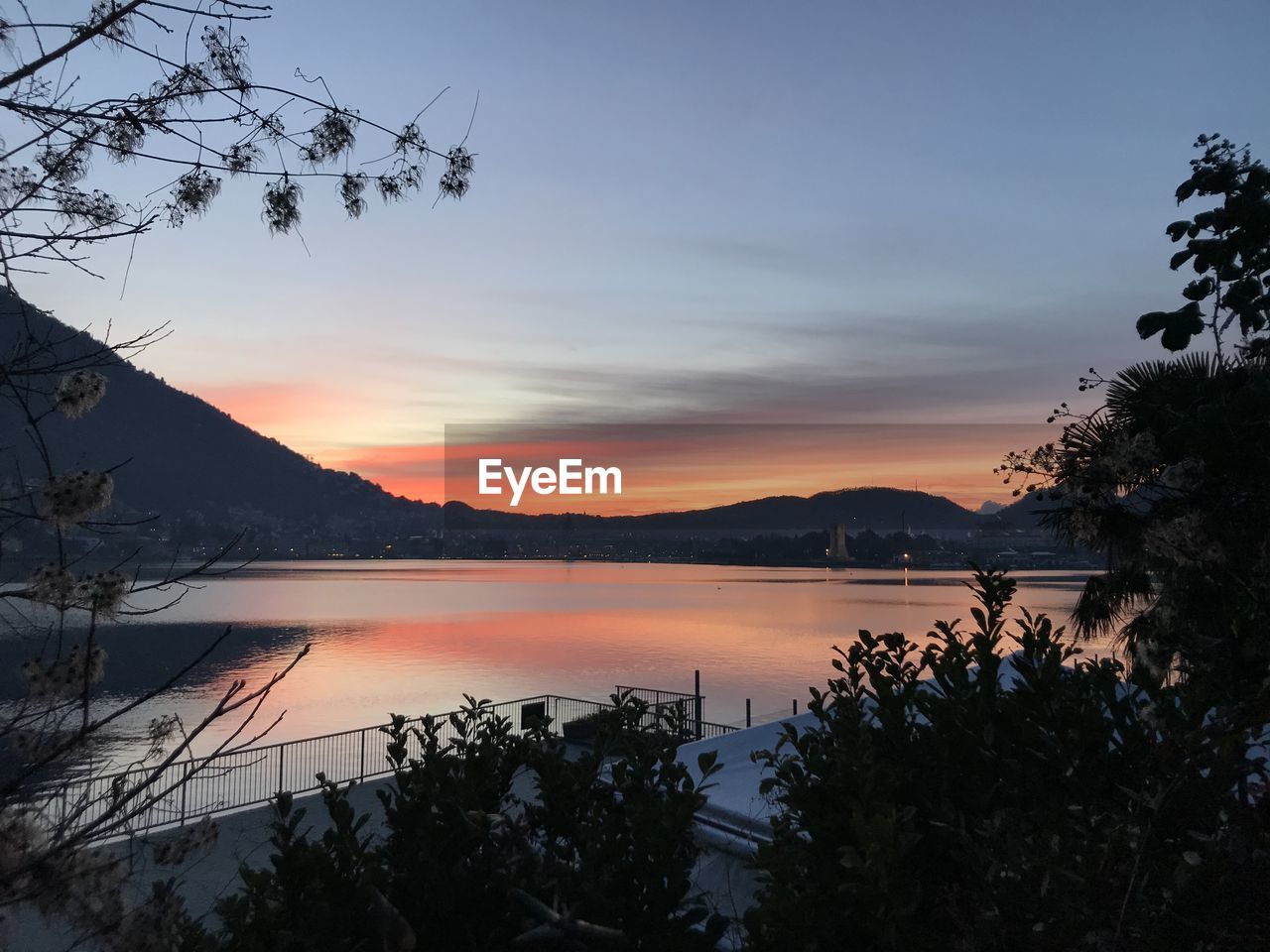 SCENIC VIEW OF LAKE BY SILHOUETTE TREES AGAINST SKY AT SUNSET