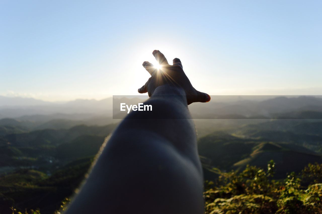 Cropped image of person hand reaching towards sun