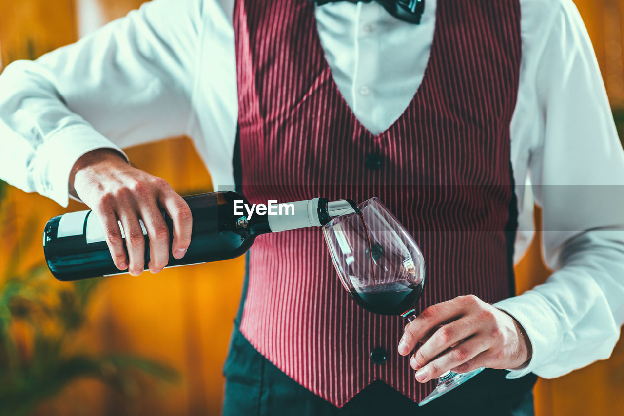 Midsection of man pouring wine in wineglass